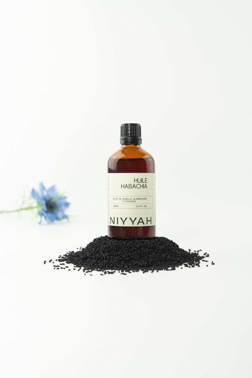Huile de nigelle Habacha d'Éthiopie 100ml alimentaire posée sur tas de graines de nigelle noires avec fleur bleue