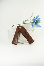 Peigne à barbe pliable NIYYAH en bois foncé – accessoire de coiffage anti statique - arrière plan claire avec fleur